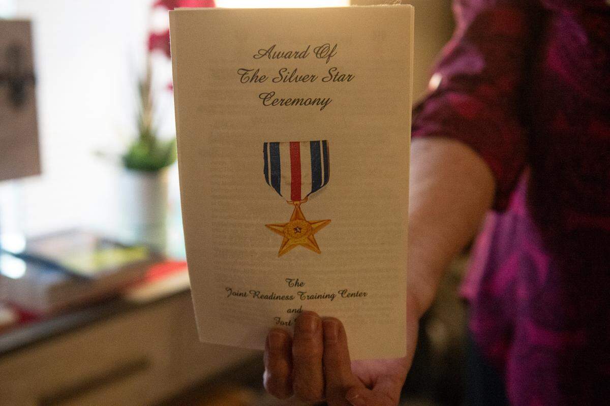 Deborah Tainsh, an author and gold star mother, holds up the program from the Silver Star ceremony for her son, Patrick, at her home in Biloxi on Wednesday, Nov. 8, 2023. Patrick, who died fighting in Iraq, inspired her to write.