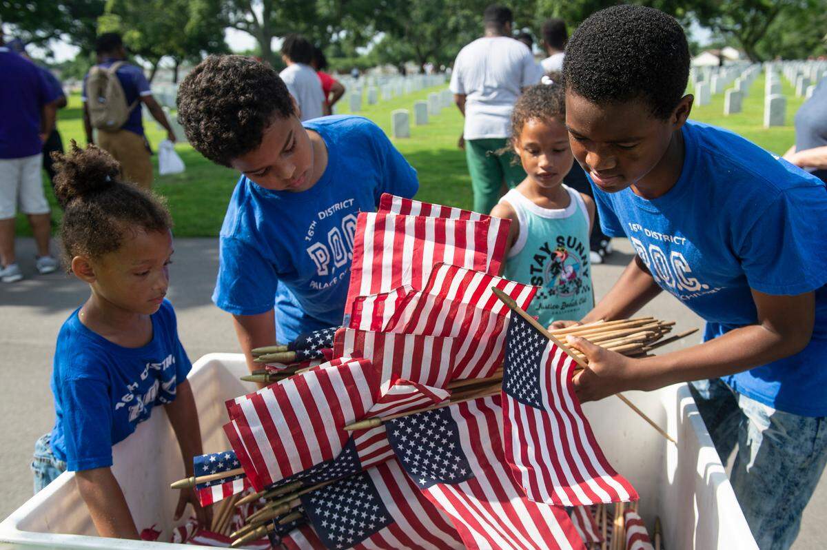 Volunteers return leftover flags after helping to place thousands of tiny American flags on the graves of American service members at Biloxi National Cemetery in Biloxi ahead of Memorial Day on Saturday, May 25, 2024.