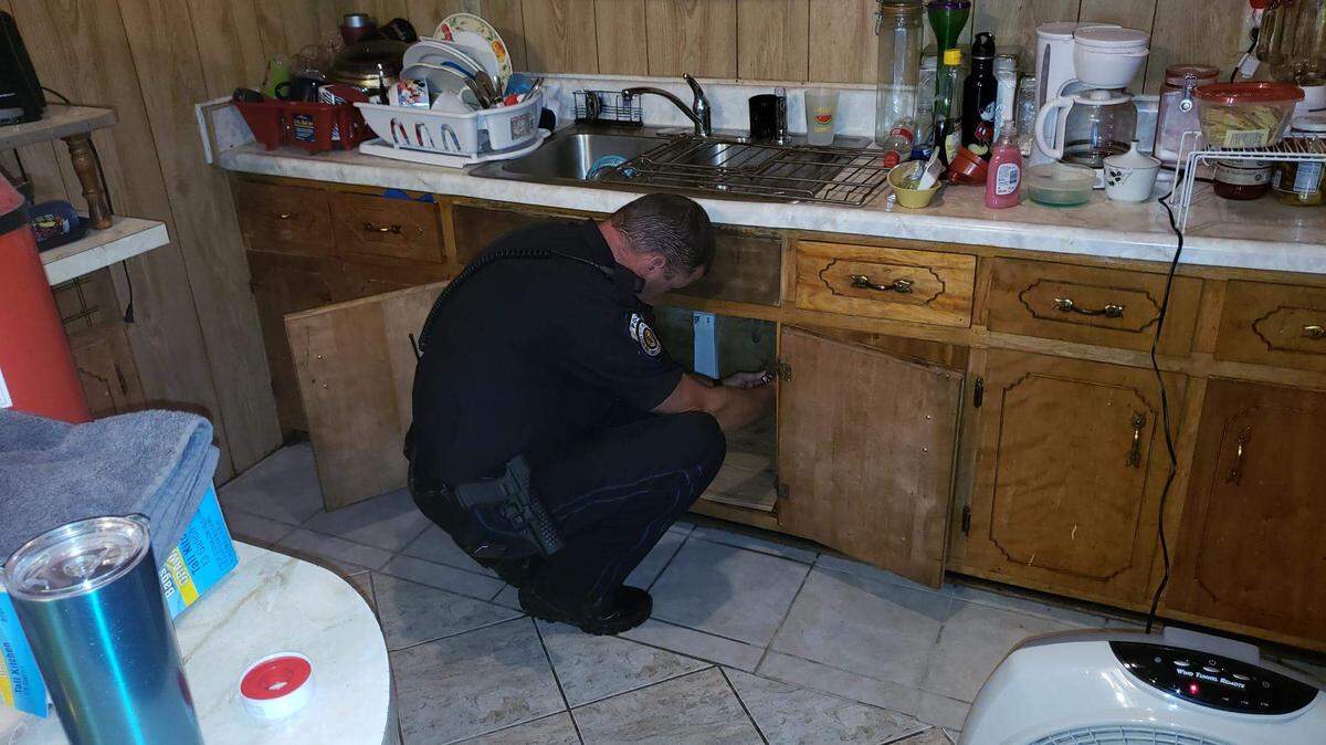 Officer Robert Hammac works on the busted pipe under the kitchen sink on Thursday as Moss Point officers responded to a woman’s emergency.