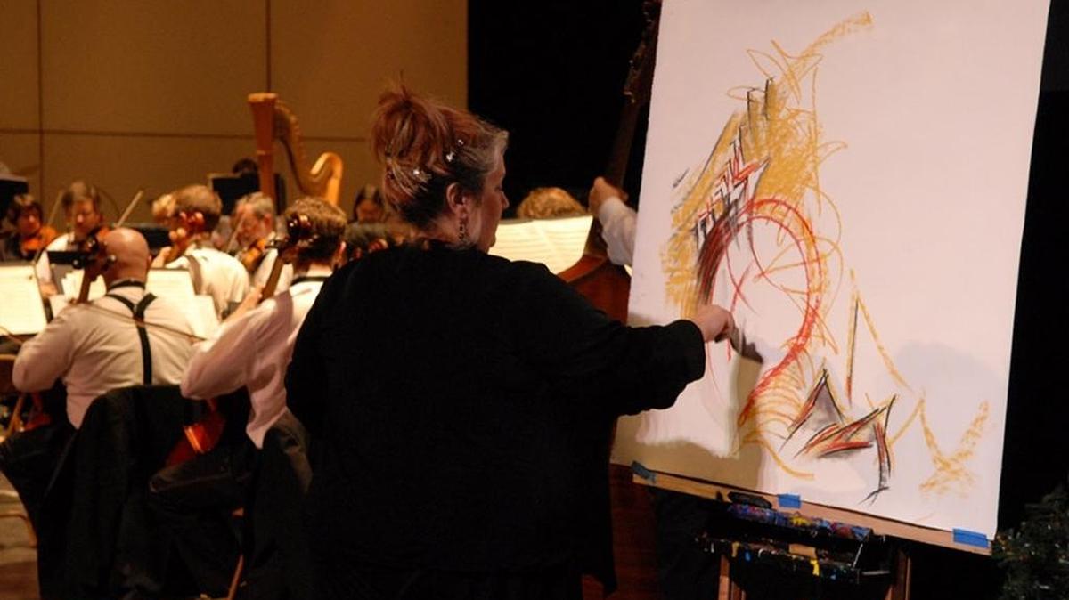 Elizabeth Shafer paints on stage as an orchestra plays