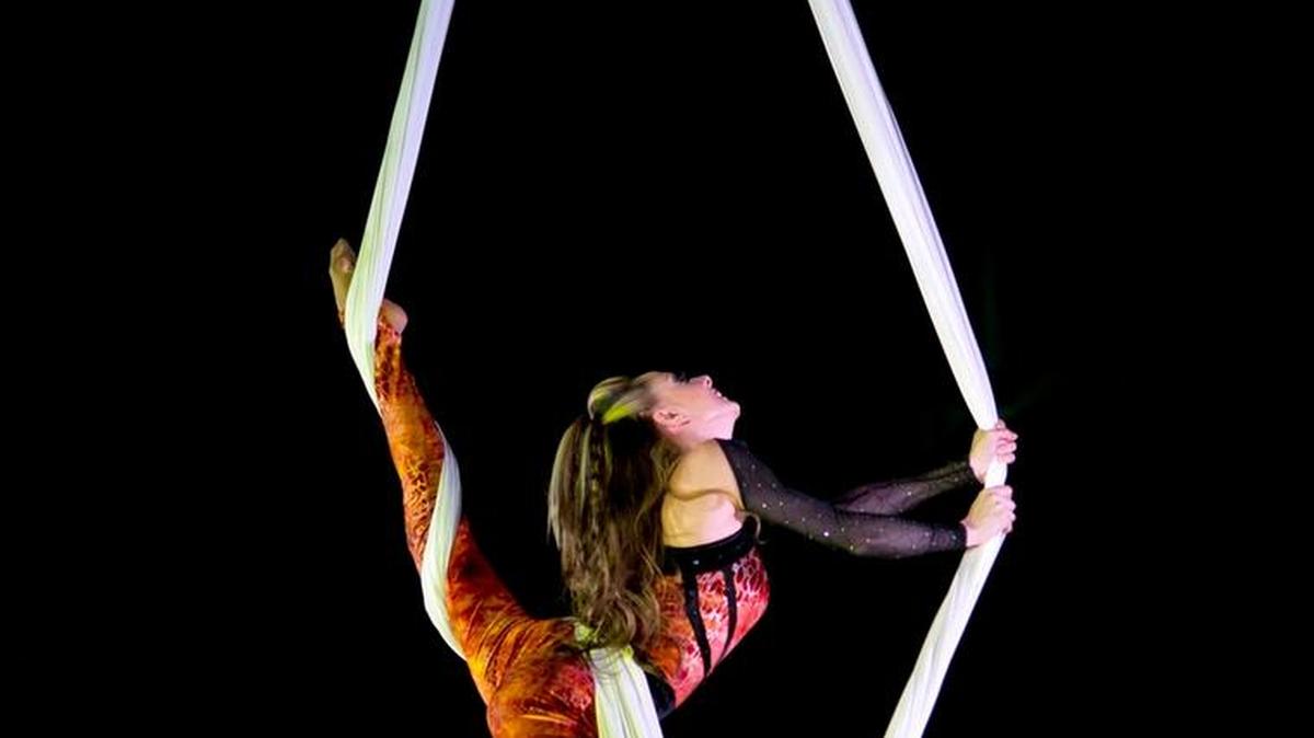 An aerialist contorts high above the ground on a chiffon.