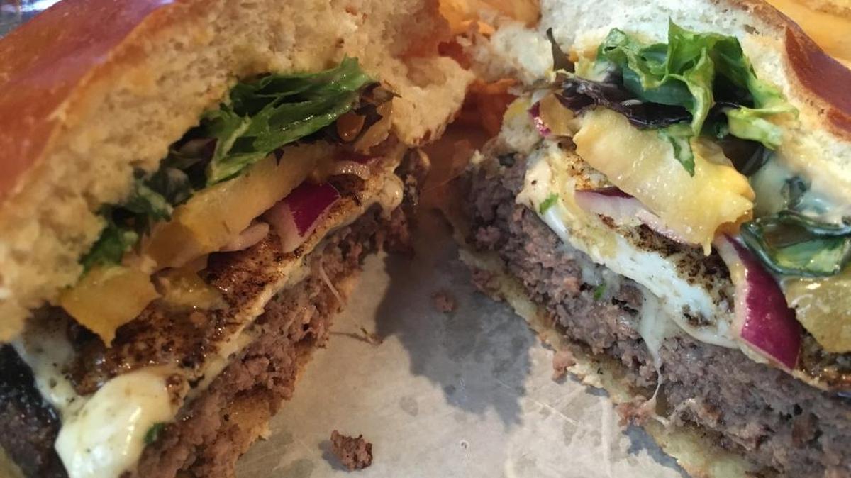 A cross-section of the Farm House burger at 27th Avenue Burger Bar in Gulfport shows the organic beef patty topped with fried egg, bacon, comeback sauce, arugula, heirloom tomato, red onion, mustard and cheese, all in a potato bun. The burger is served with house-made chips.