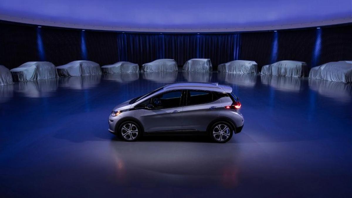 A Chevrolet Bolt, surrounded by nine electric and fuel cell vehicles covered by tarps.