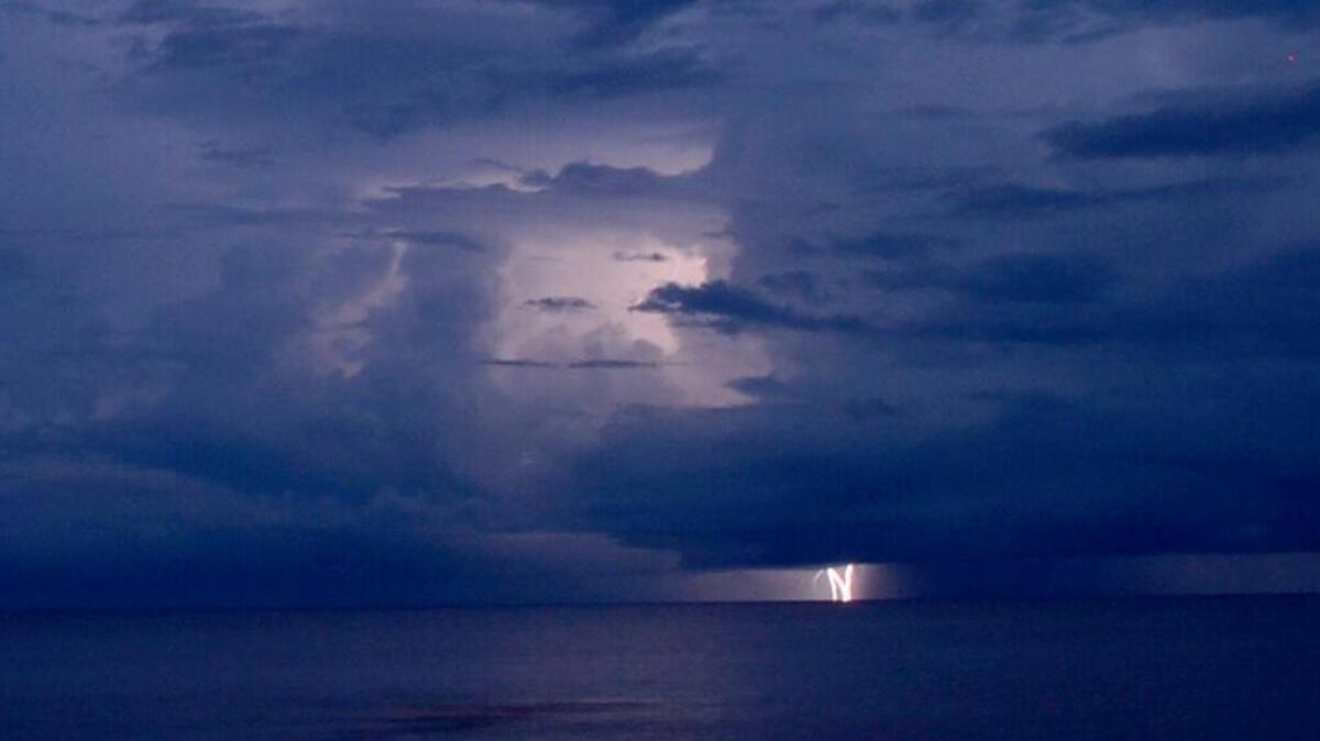 On an otherwise dark night, huge clouds are illuminated by flashes of lightning as a lone streak appears on the horizon, in Biloxi, Friday, July 14, 2017.