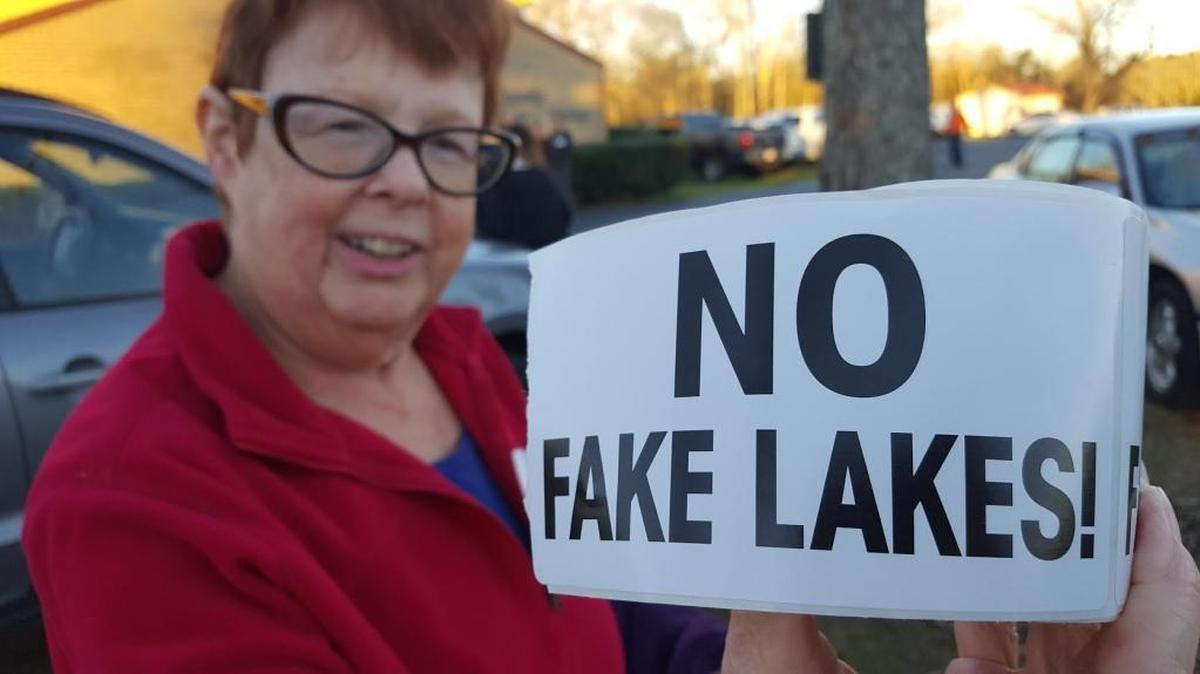 Jeanne Lebow, a retired Coast teacher, helps her husband pass out stickers for the meeting.