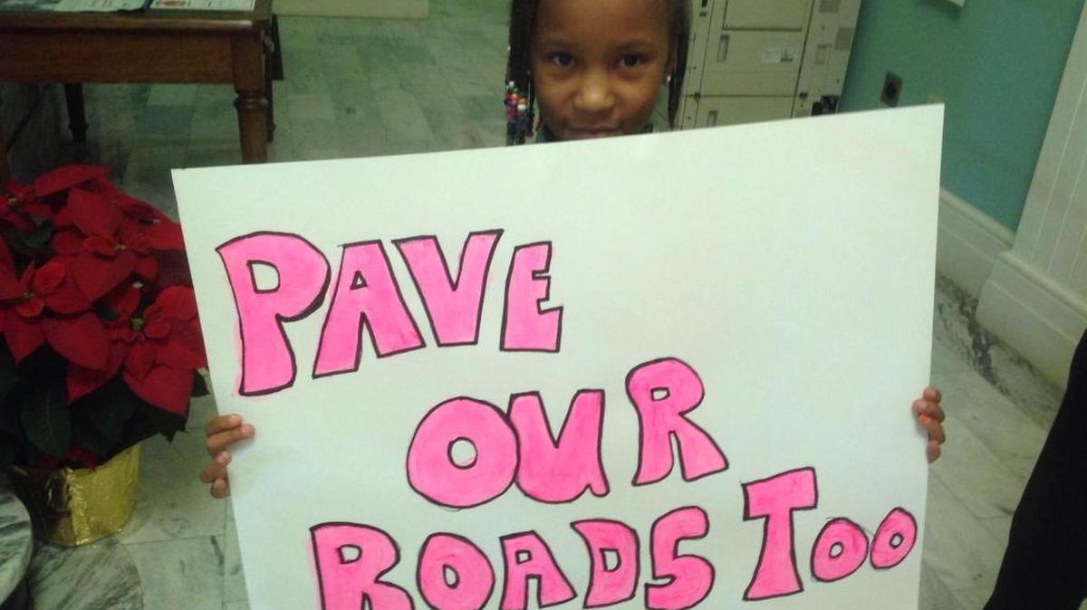 Gabryelle Eason holds a sign outside the Biloxi council meeting Tuesday asking for the city to do something about the roads in East Biloxi.