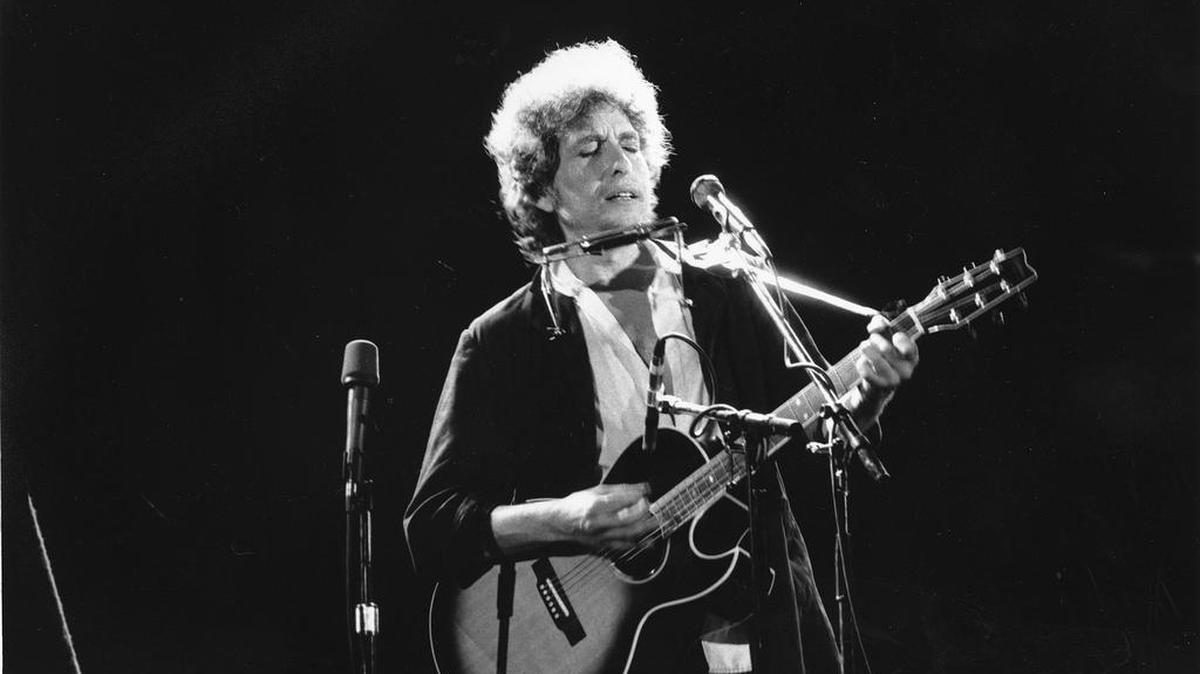 This is an undated photo of singer-songwriter Bob Dylan as he plays his acoustic guitar with his harmonica at an unknown location.
