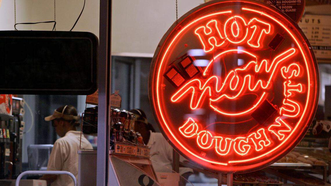 Employees work in the shadow of a “Hot Doughnuts Now” sign at a Krispy Kreme store is shown in Matthews, N.C., early Friday, Sept. 7, 2007. (AP Photo/Chuck Burton)