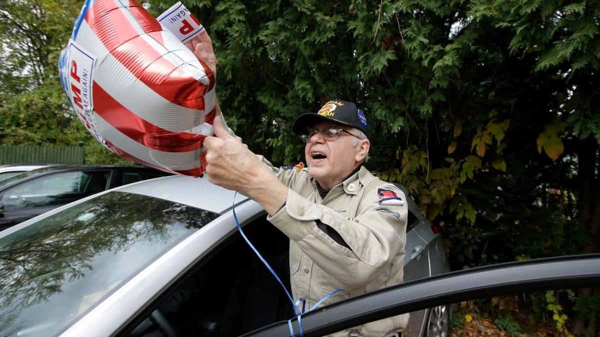 Norm DeLap, of Webster, Mass., a U.S. Army Vietnam veteran, and supporter of Donald Trump, attaches a Trump sticker to a balloon as he arrives at a campaign stop for Republican vice presidential candidate, Indiana Gov. Mike Pence, in Rochester, N.H., Sunday, Oct. 30, 2016.