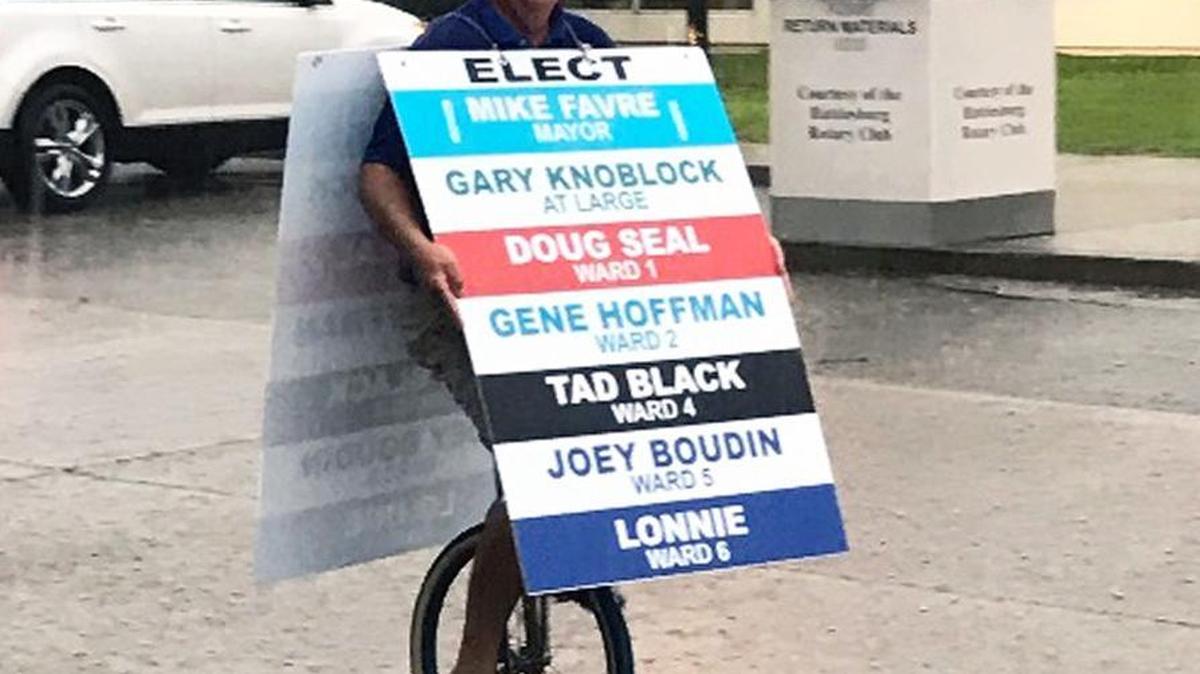 Mayoral candidate Jeff Harding rides a unicycle in the rain while wearing a sign to elect opponent Mike Favre, who won the seat.