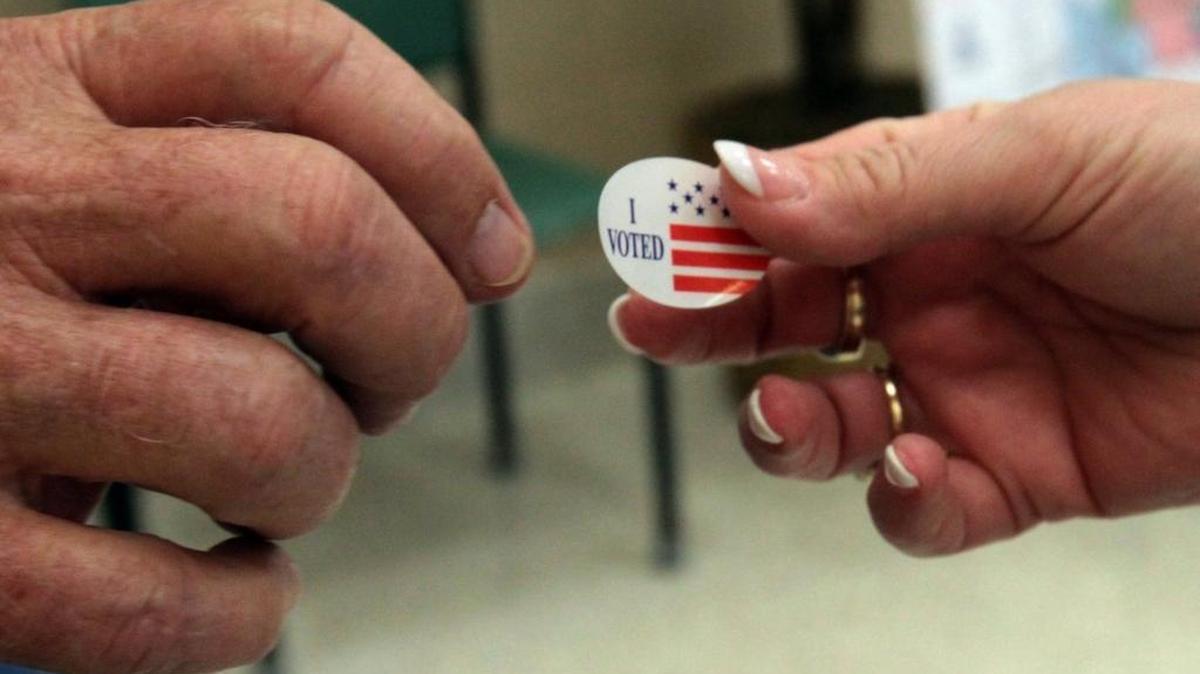 Roy Moyle hands a ‘I Voted’ sticker to a citizen after voting in the Biloxi municipal elections at Donal Snyder Community Center in Biloxi on May 7, 2013.