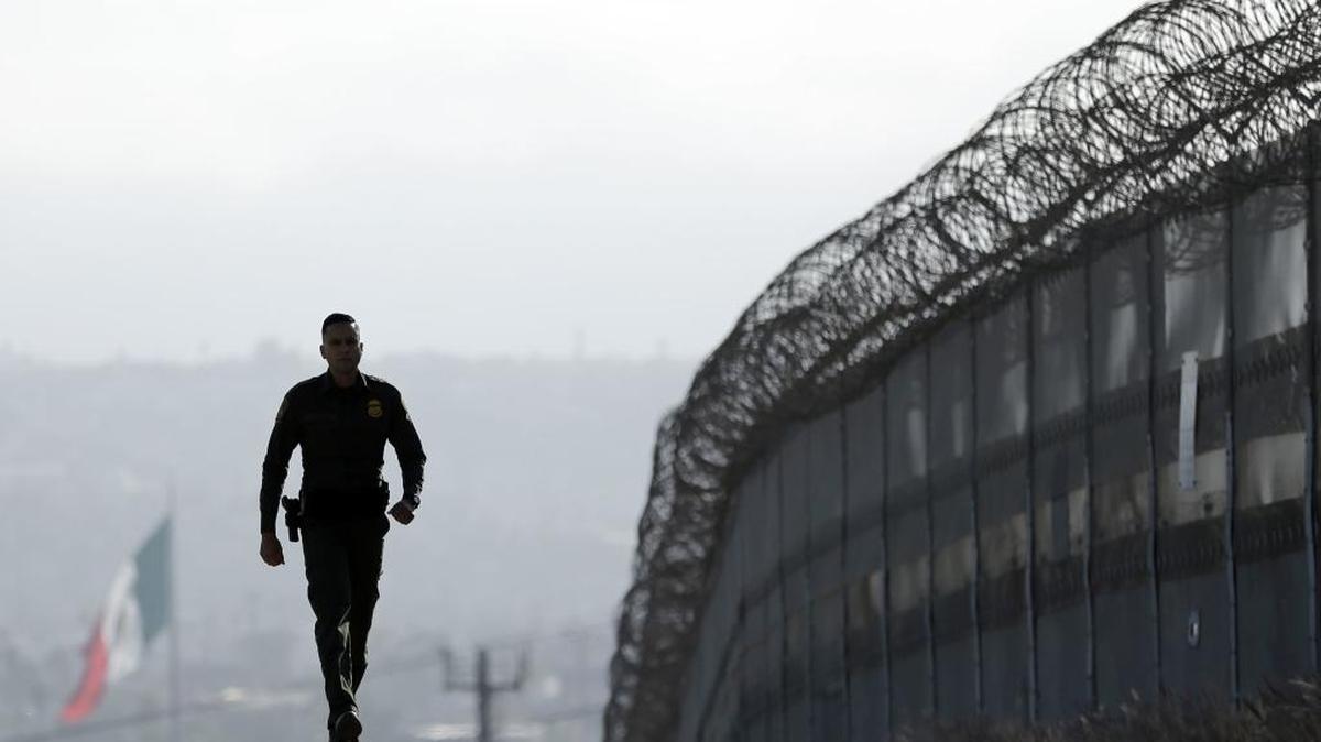 Border Patrol agent Eduardo Olmos walks near the secondary fence separating Tijuana, Mexico, background, and San Diego in San Diego.