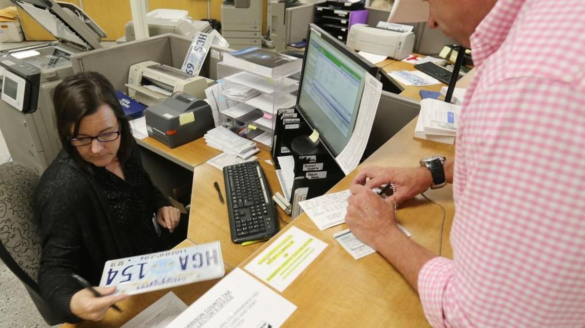 Ken Berry writes a check for his car tag as deputy clerk Sherry Hill processes it at the Harrison County Tax Collector's office at the county courthouse in Gulfport on Tuesday, Feb. 27, 2018.