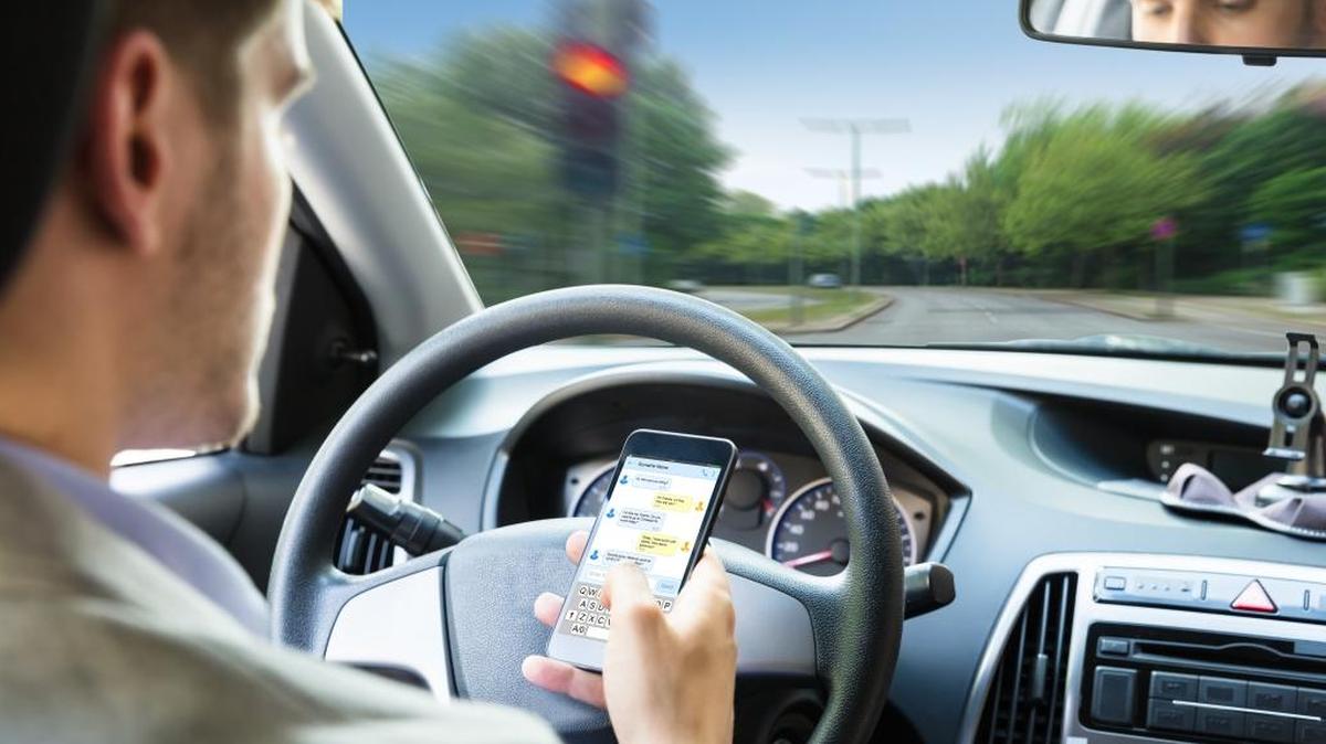 Close-up Of A Person’s Hand Sending Text Message By Mobile Phone While Driving Car