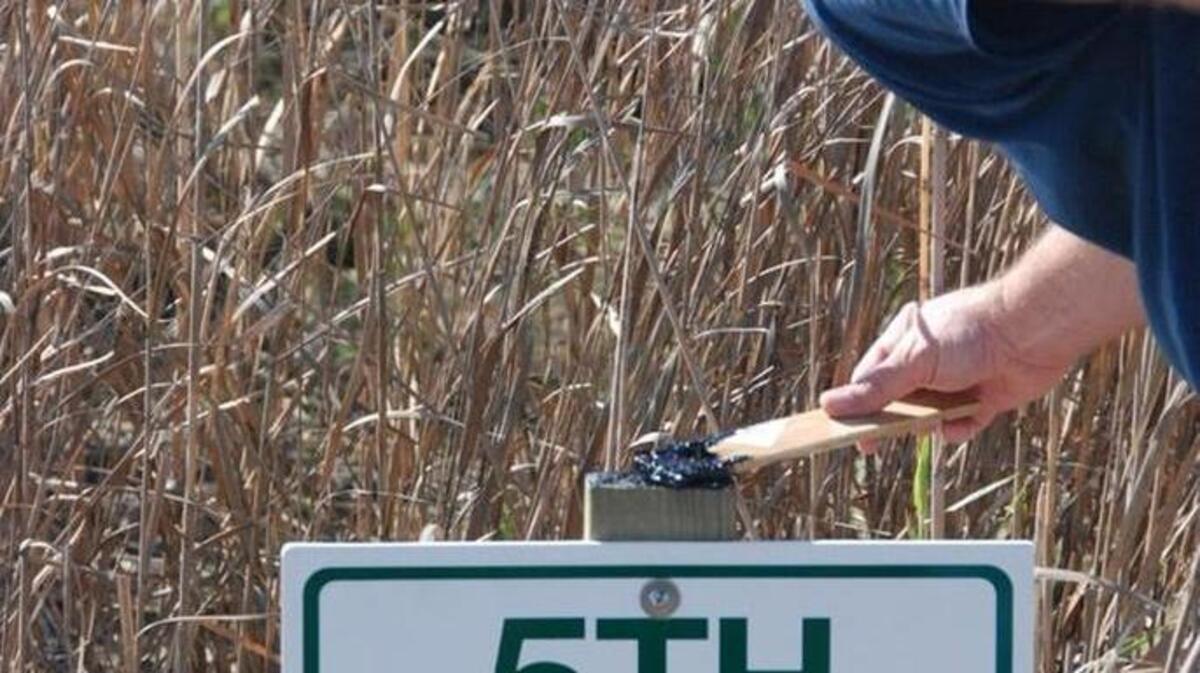 Thomas Robertson coats the top of the wooden sign post for 5th Bayou to prevent rot.