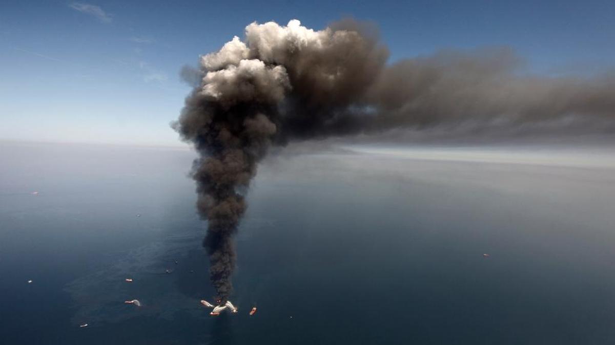 In April 2010, oil can be seen in the Gulf of Mexico, south of Gulfport, as a large plume of smoke rises from fires on BP’s Deepwater Horizon offshore oil rig.
