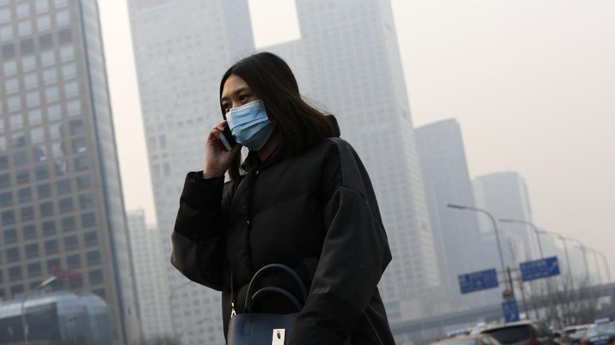 A woman wearing a mask to protect herself from pollutants walks past office buildings shrouded with pollution haze in Beijing, the capital of China, in December 2015.