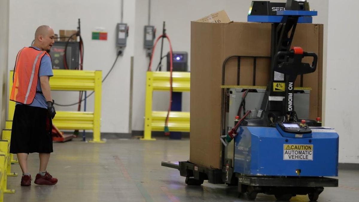 An employee looks on as a robot carries packages at the Amazon Fulfillment center in Robbinsville Township, N.J., Wednesday, Aug. 2, 2017.