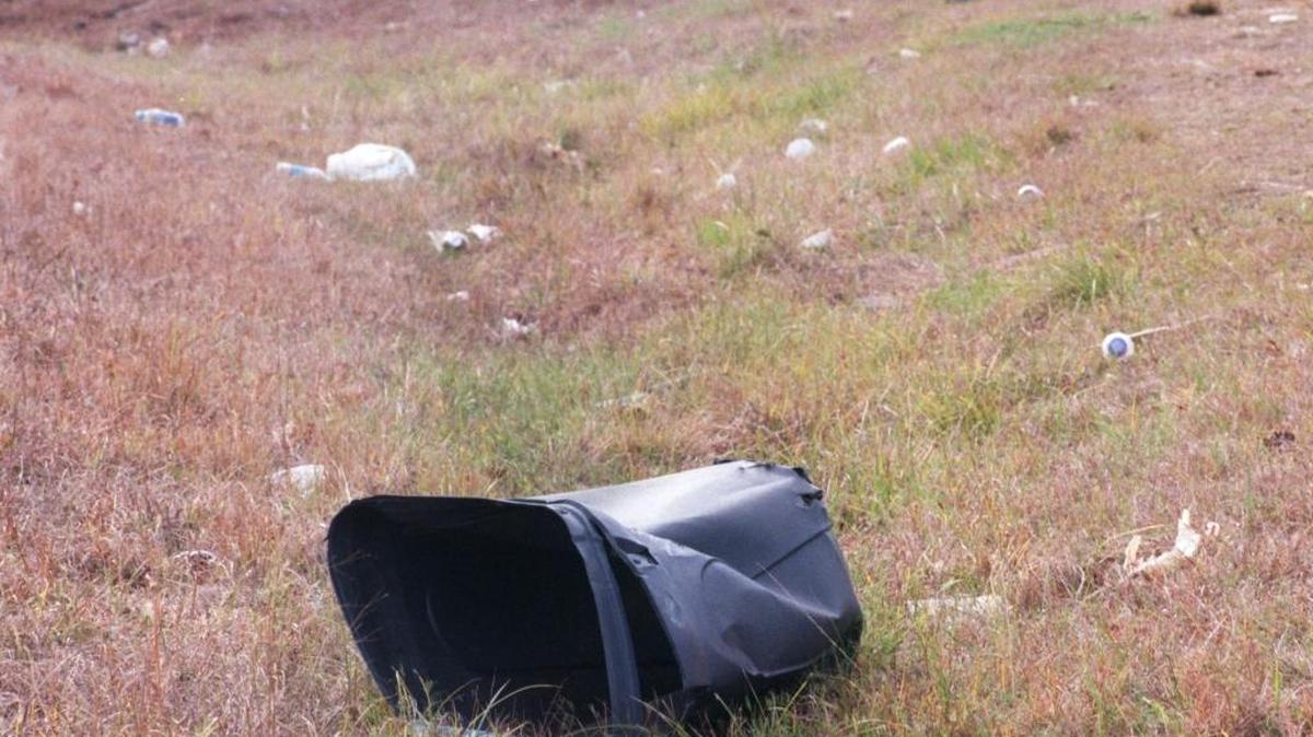 A discarded trash can along litters the side of Old Highway 67 along with lots of other trash.