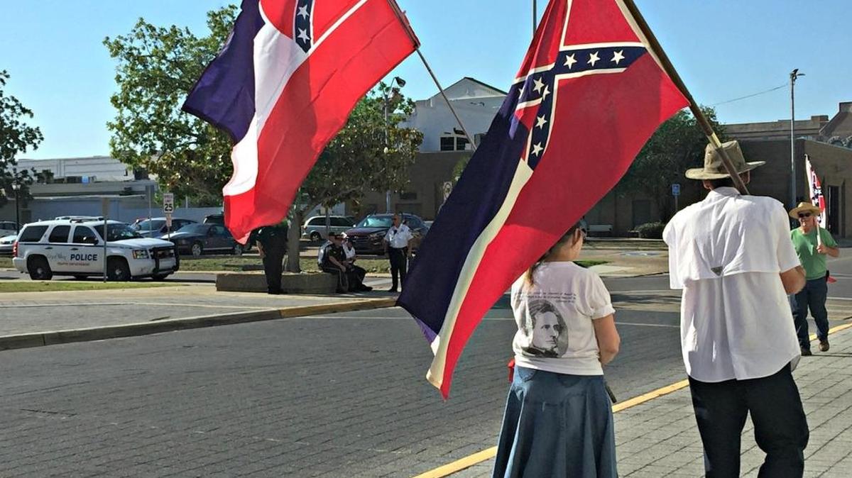 People carry the Mississippi flag outside Biloxi City Hall on May 29, while across the street Biloxi Police keep watch.