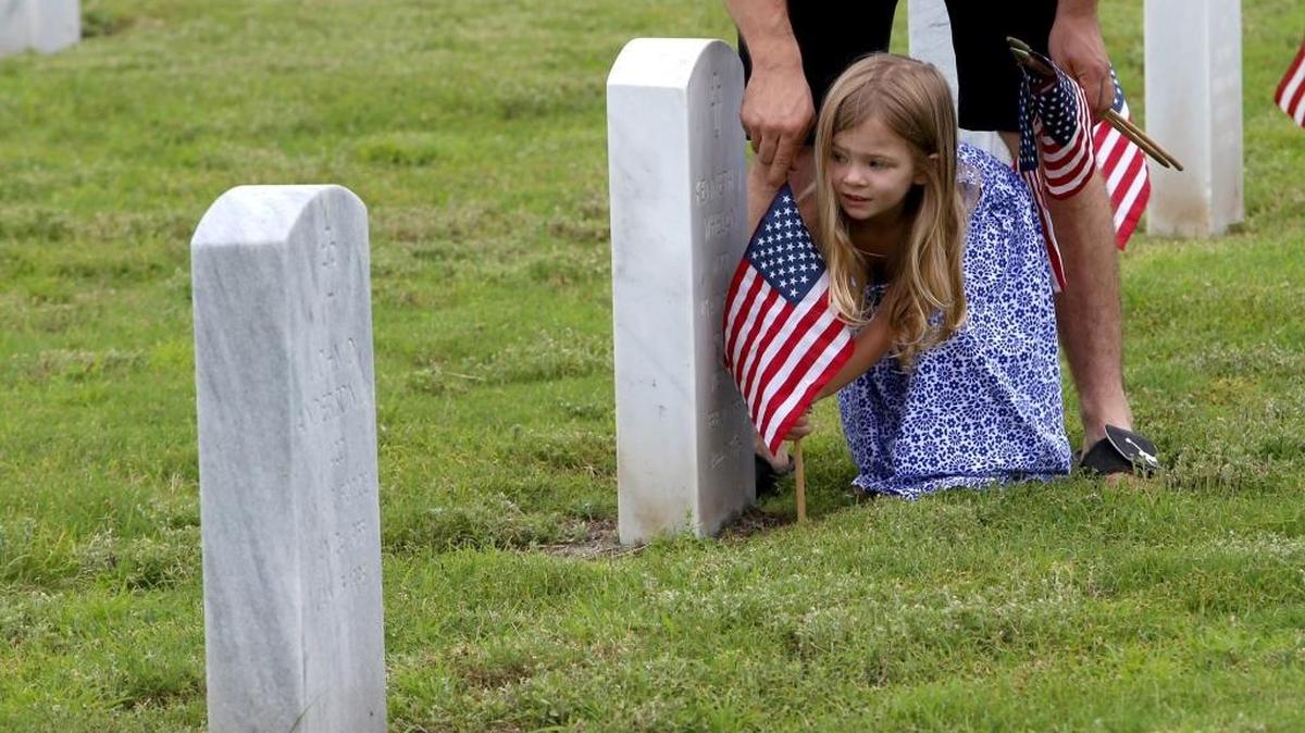 Mya Brackett gets some help from her father, Michael Brackett, as they place flags on graves at the Biloxi National Cemetery, Saturday, May 27, 2017.