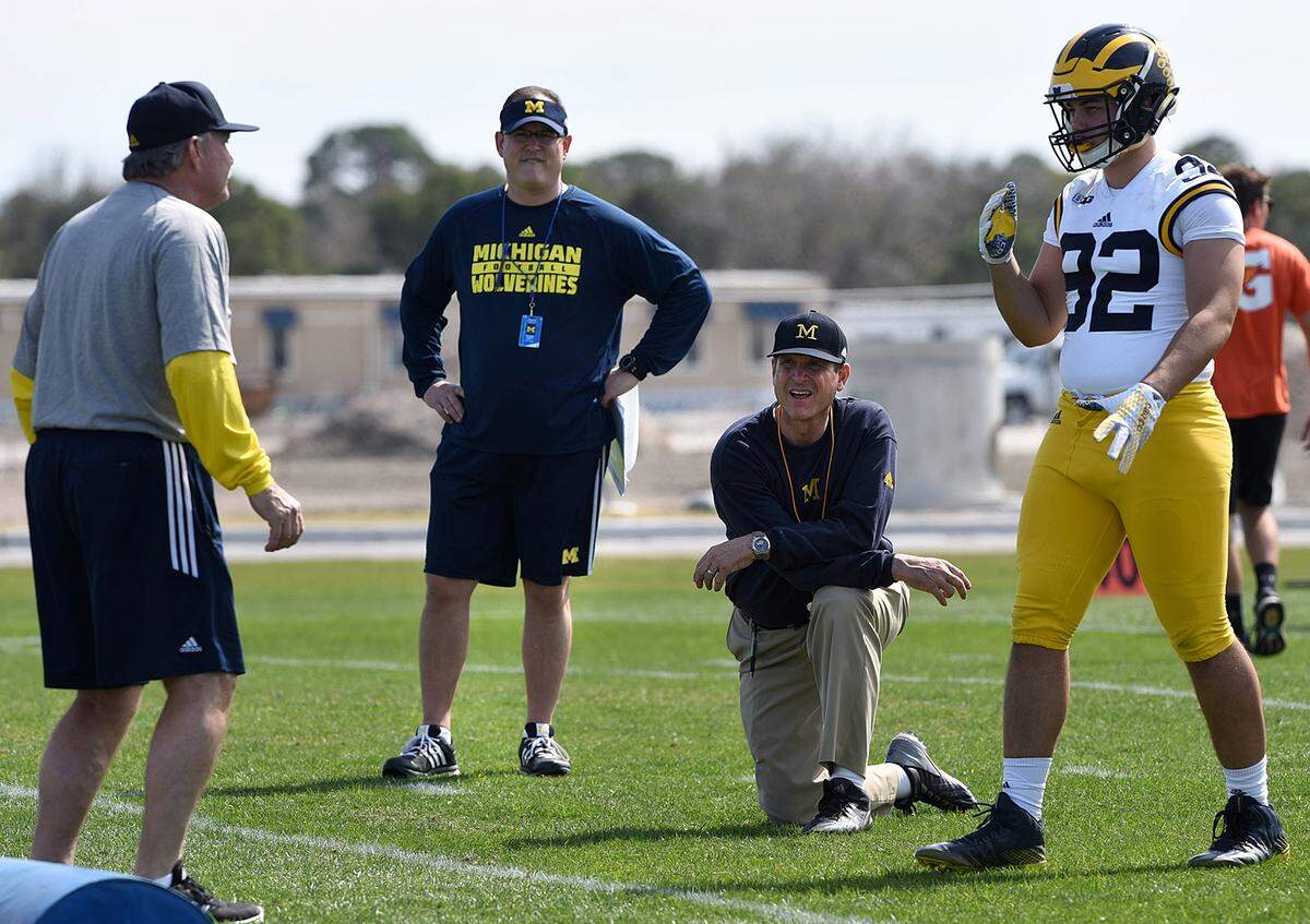 FILE - In this Feb. 29, 2016, file photo, Michigan's head coach Jim Harbaugh, center right, watches defensive coordinator Don Brown, left, work with Cheyenn Robertson during team practice in Bradenton, Fla. The NCAA announced Friday, April 8, 2016, that it was barring football coaches from holding camps or clinics on other campuses, siding with the Southeastern Conference in its high-profile dispute with Michigan's Jim Harbaugh. 