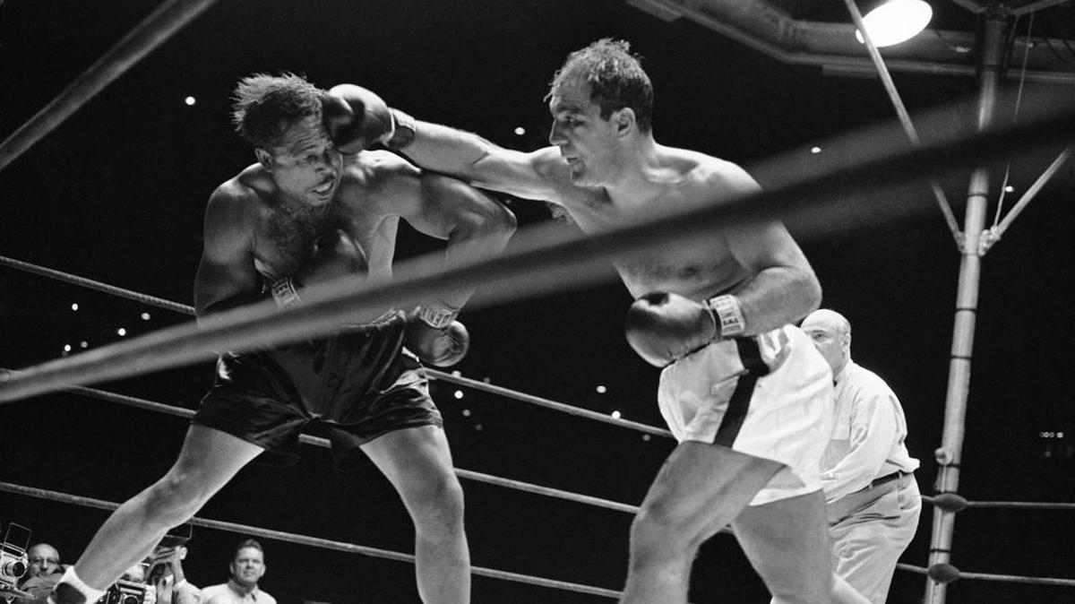 Heavyweight champion Rocky Marciano’s right fist made challenger Archie Moore’s hair stand on end-like this-more than once during their title bout at Yankee Stadium in New York City, Sept. 21, 1955. Marciano retained his crown when he dropped Moore by a knockout in the ninth round of their scheduled 15-round bout. Note how Moore’s gloves are well away from punch in this action.